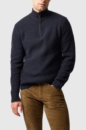 A man wearing the Rodd & Gunn Robbies Road Knit quarter-zip sweater and brown corduroy pants stands against a light gray background, his head slightly tilted down with one hand in his pocket.