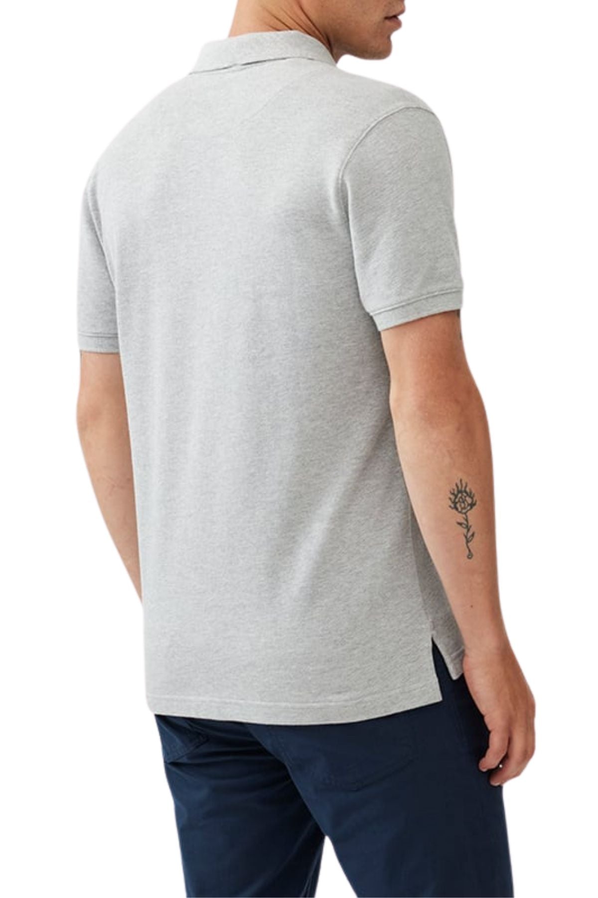 A person is shown from the back wearing a light gray Rodd & Gunn The Gunn Polo styled casually with navy pants, revealing a small sun tattoo on their right forearm.