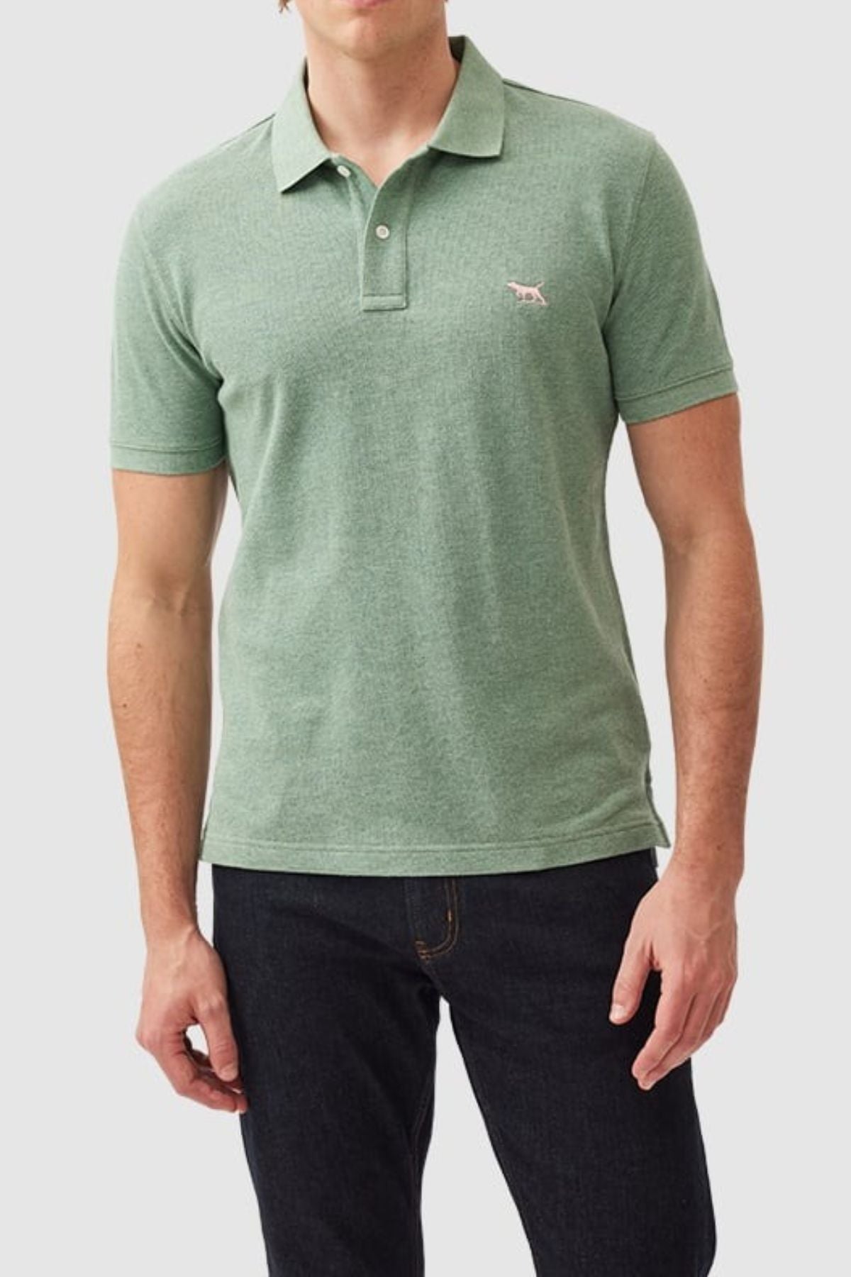 A person wears the Rodd & Gunn The Gunn Polo, a modern fit, light green polo shirt crafted from Australian cotton with a small embroidered animal logo on the chest, paired with dark jeans against a plain, light-colored background.