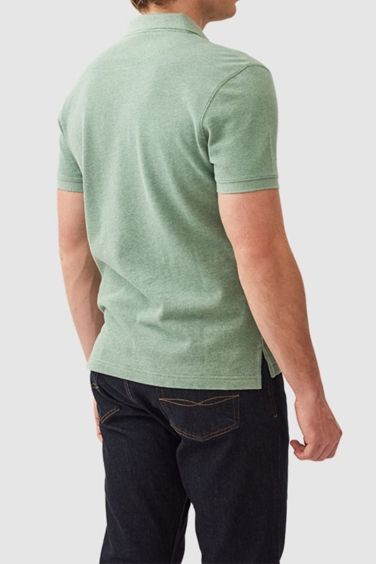 A person in a Rodd & Gunn The Gunn Polo, green modern-fit and crafted from Australian cotton, paired with dark jeans, is seen from behind against a plain light gray backdrop.