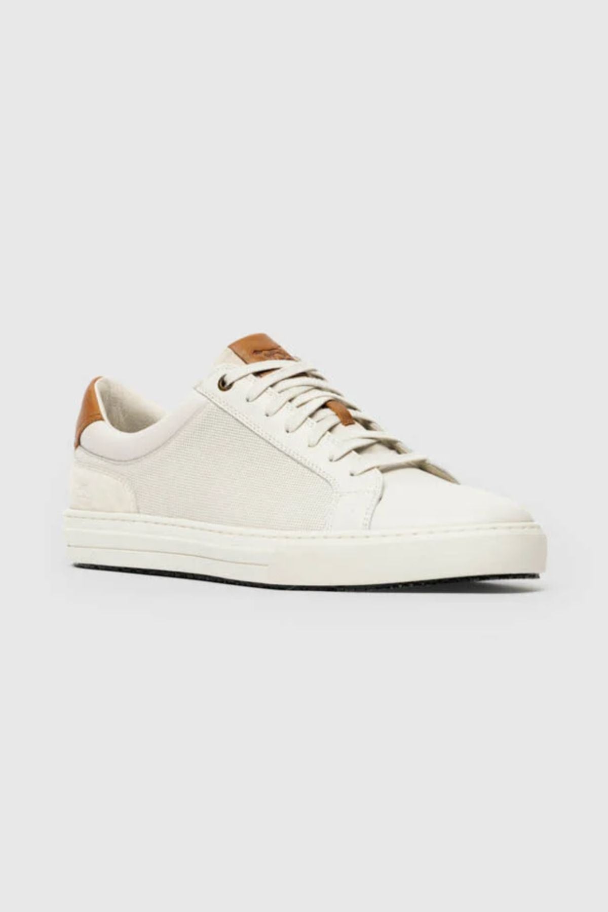 The Rodd & Gunn Transit Sneaker is a low-top white shoe with a canvas upper, white laces, and tan premium leather accents on the tongue and heel, displayed against a plain light gray background.