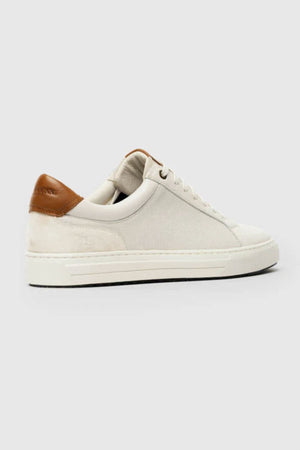 The Rodd & Gunn Transit Sneaker is a white low-top made from high-quality leather, with a brown leather heel accent, white laces, and a cream sole, shown against a light gray background.