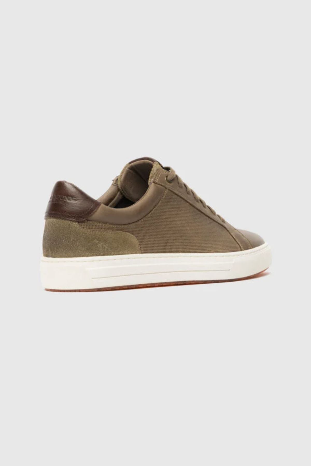 The Rodd & Gunn Transit Sneaker is a brown low-top leather shoe with suede heel accents and a white sole, displayed on a light gray background. Refined details give it a timeless, classic look.