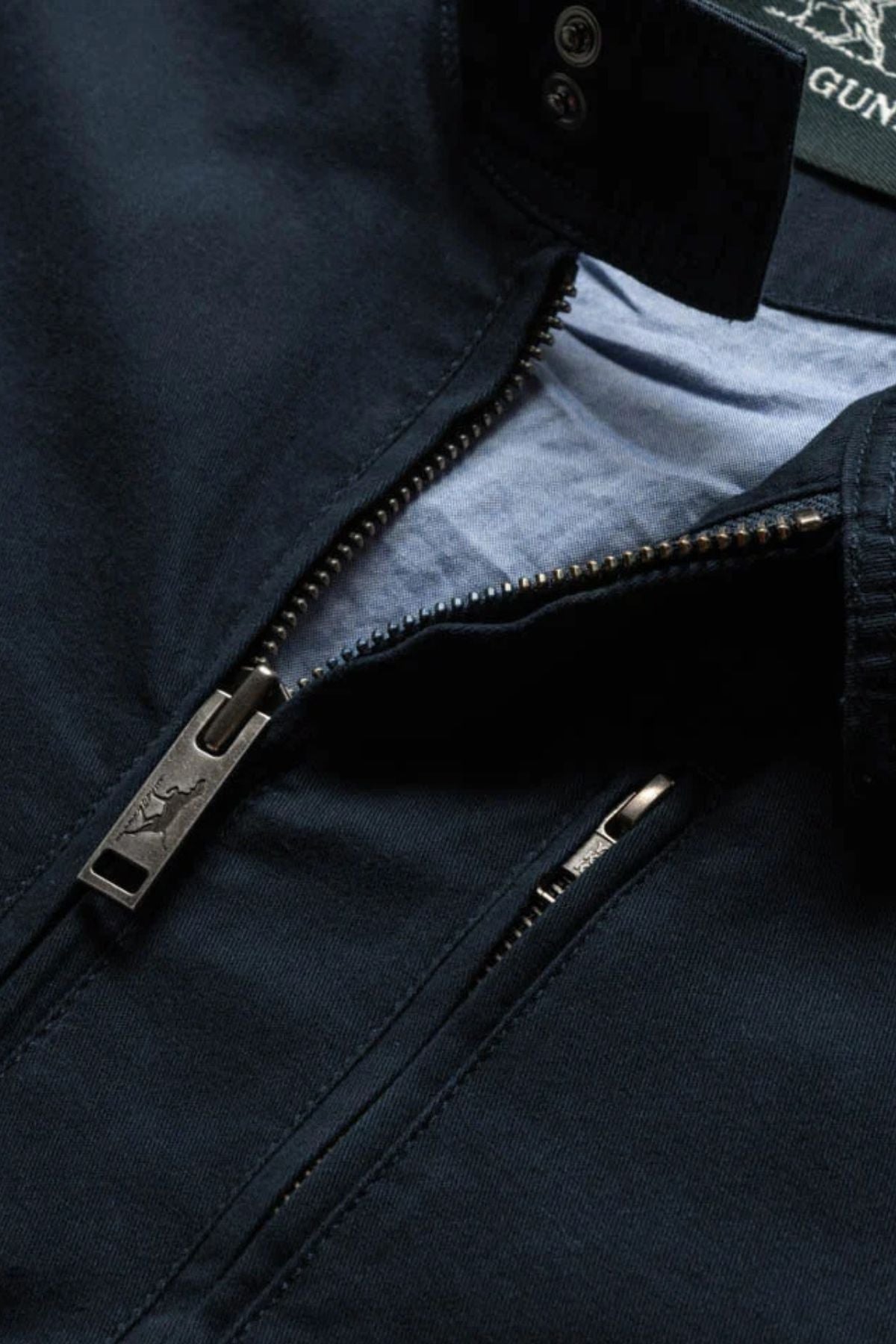 Close-up of the Rodd & Gunn Armitage Jacket for men in navy blue, featuring a partially unzipped zipper that reveals a light blue Australian Cotton lining and a branded zipper pull.