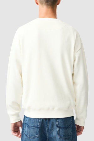 A person stands with their back to the camera, wearing the Rodd & Gunn Bromley Sweat and blue jeans, set against a light gray background.