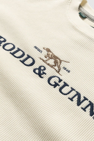 Close-up of the cream-colored Rodd & Gunn Bromley Sweat, showcasing "RODD & GUNN" embroidered in dark blue, a brown dog logo with "REGD 1946" above—made as a sustainable sweatshirt from recycled polyester.