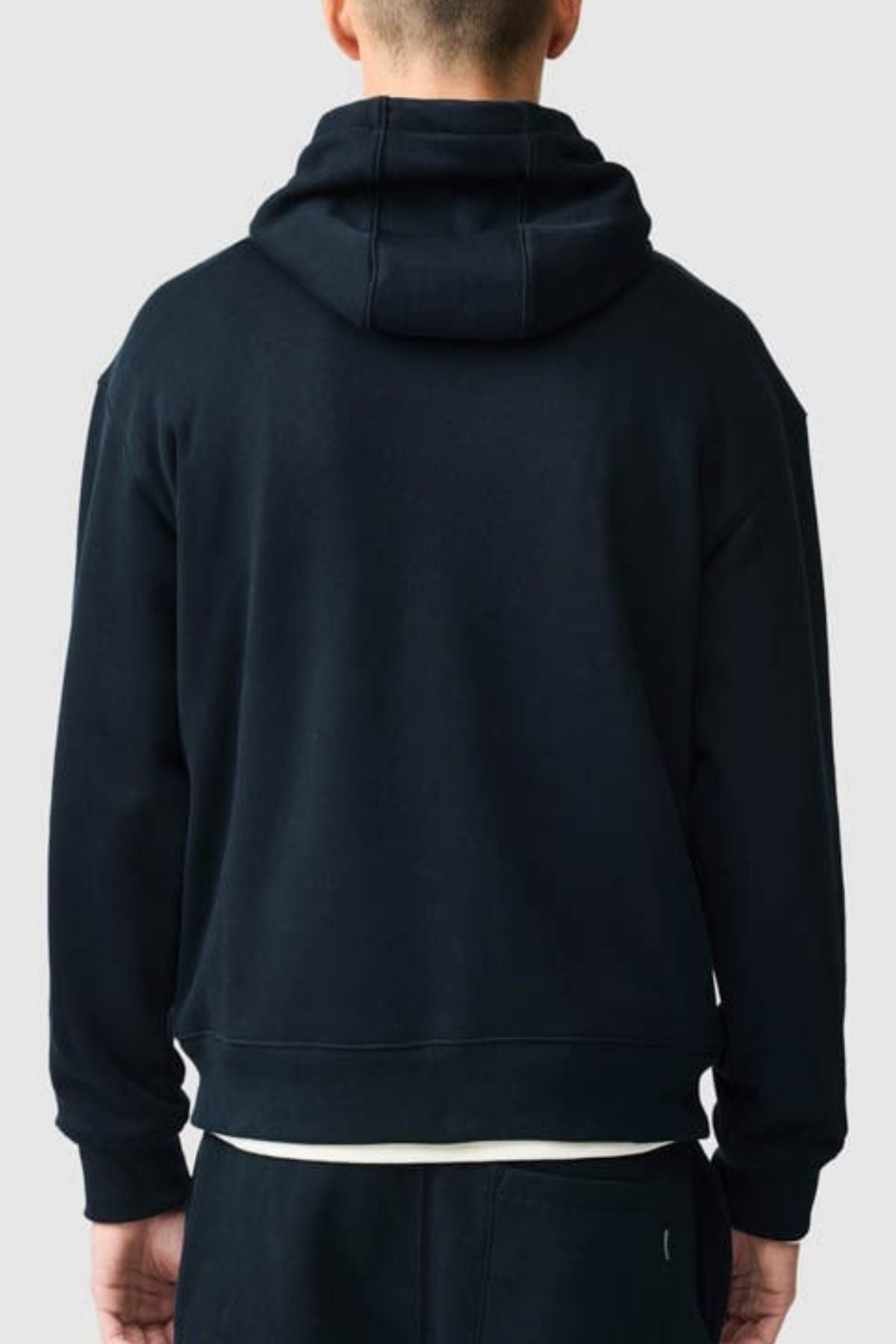 A person wearing a black Rodd & Gunn Otago Hoodie made from Australian cotton is shown from the back, with the hood down and their hands by their sides, against a plain light gray background.