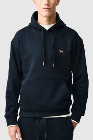 Wearing the Rodd & Gunn Otago Hoodie in black, crafted from soft Australian cotton and adorned with a small embroidered animal logo on the left chest, paired with matching black pants, a person stands against a plain light background.