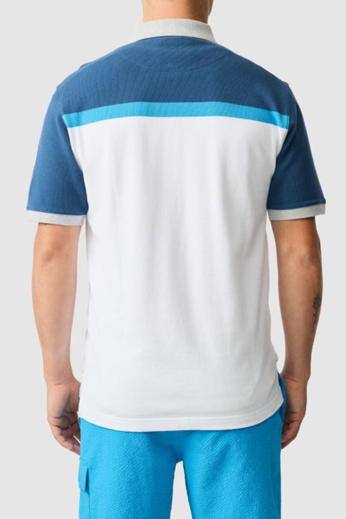 Someone models the Rodd & Gunn Whitby Polo with a blue and white color block design and light gray trim, paired with bright blue shorts, as they are photographed from the back against a simple light background.