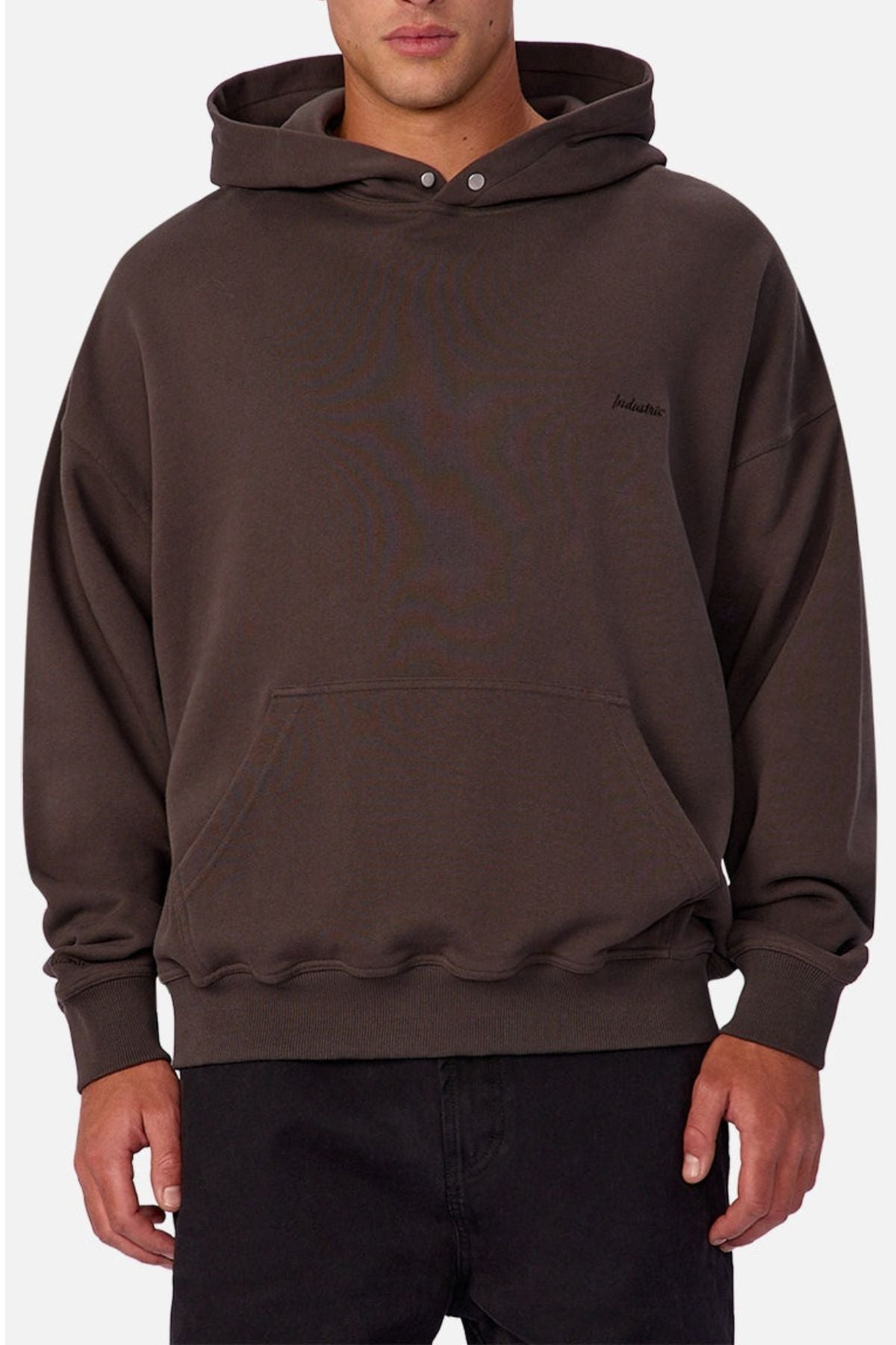 A person wearing a loose-fitting, dark brown Industrie The Sandblast Hoodie crafted from 100% cotton, featuring a front pocket, paired with black pants and standing against a plain white background for an effortlessly laid-back style.