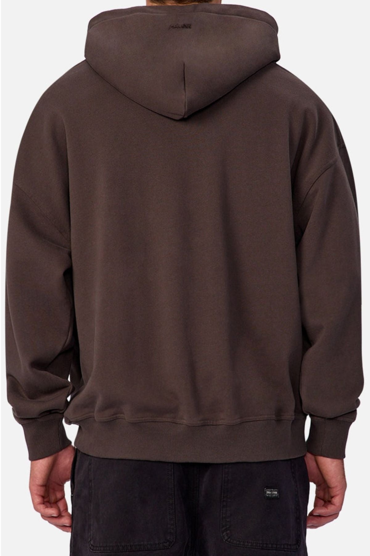 A person is shown from behind wearing a loose-fitting, dark brown Industrie The Sandblast Hoodie paired with dark pants. With the hood up and hands relaxed at their sides, the look emphasizes a laid-back style against a plain, light-colored background.