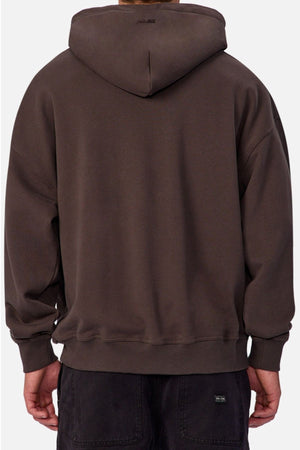 A person is shown from behind wearing a loose-fitting, dark brown Industrie The Sandblast Hoodie paired with dark pants. With the hood up and hands relaxed at their sides, the look emphasizes a laid-back style against a plain, light-colored background.