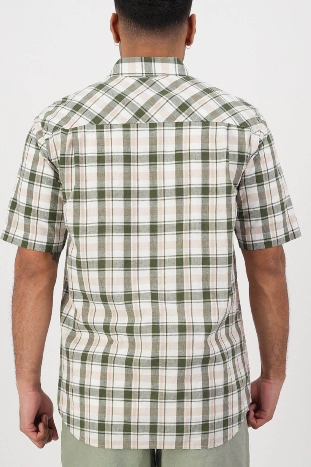 A person is shown from behind wearing the Swanndri Coleridge Short Sleeve Shirt, featuring green, white, and beige plaid stripes in a cotton linen blend. The untucked shirt is paired with light pants against a plain white background.