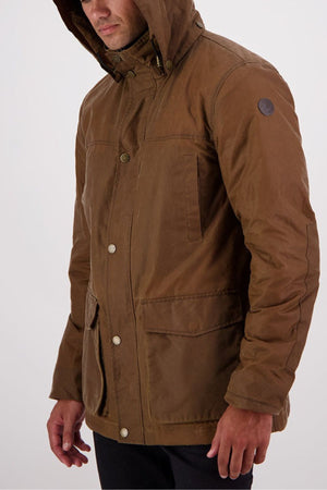 Man wearing the Swanndri Evans Flat v2 Oilskin Jacket, a brown waxed cotton hooded coat with front pockets and button closures. The fabric is subtly water-resistant. He stands against a plain light background, face partially visible as he looks downward.