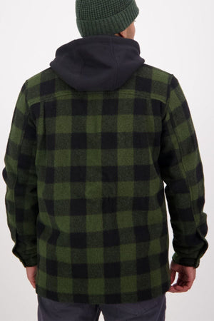A person seen from behind wears a green and black plaid Swanndri Hudson Jacket with a black hood, gray pants, and a green knit beanie. This outdoor jacket is made from soft New Zealand wool against a plain, light background.