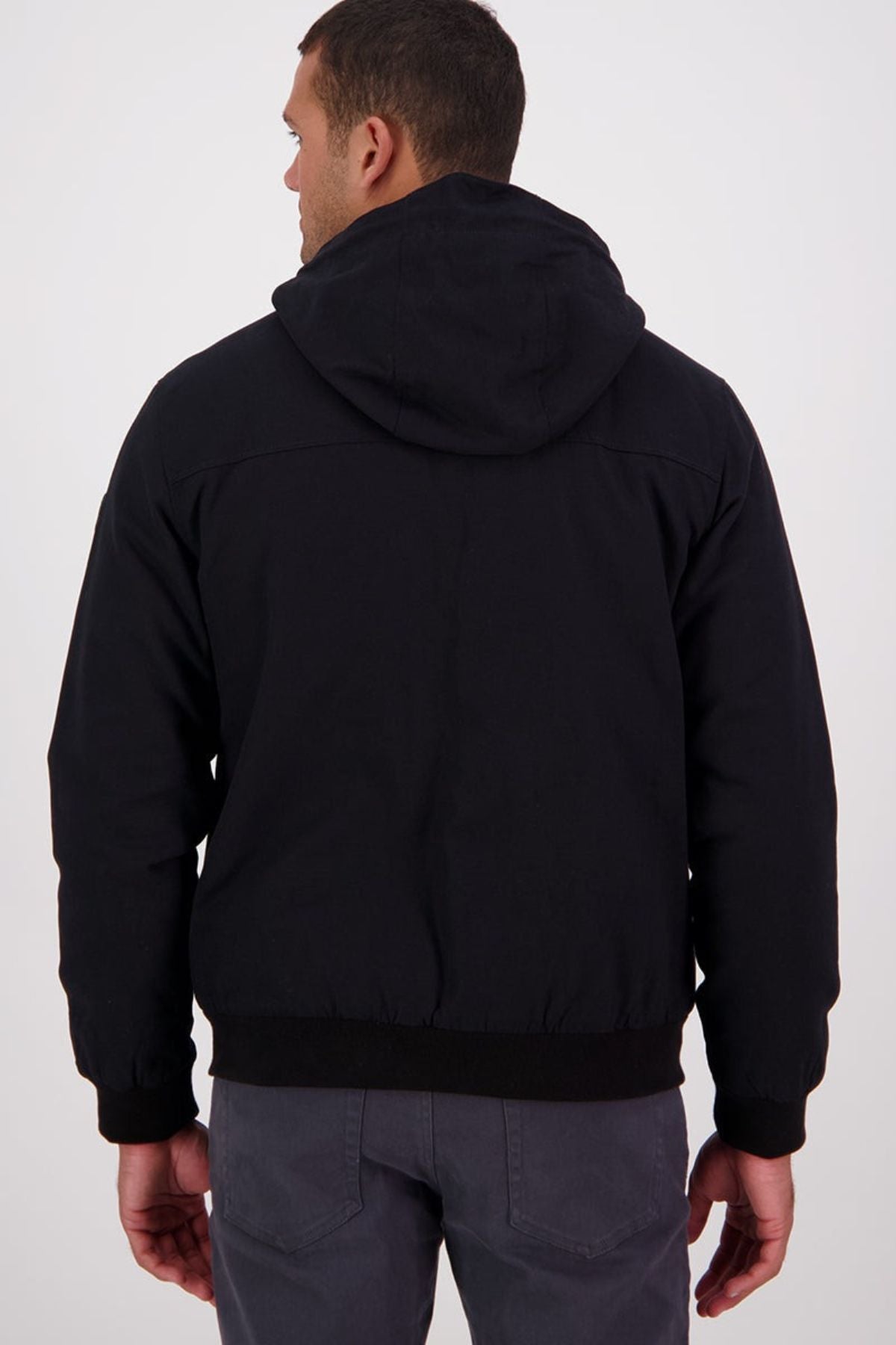A man faces away from the camera, wearing a Swanndri Whitlow v2 Canvas Hoodie in black and dark gray pants, set against a plain light background.