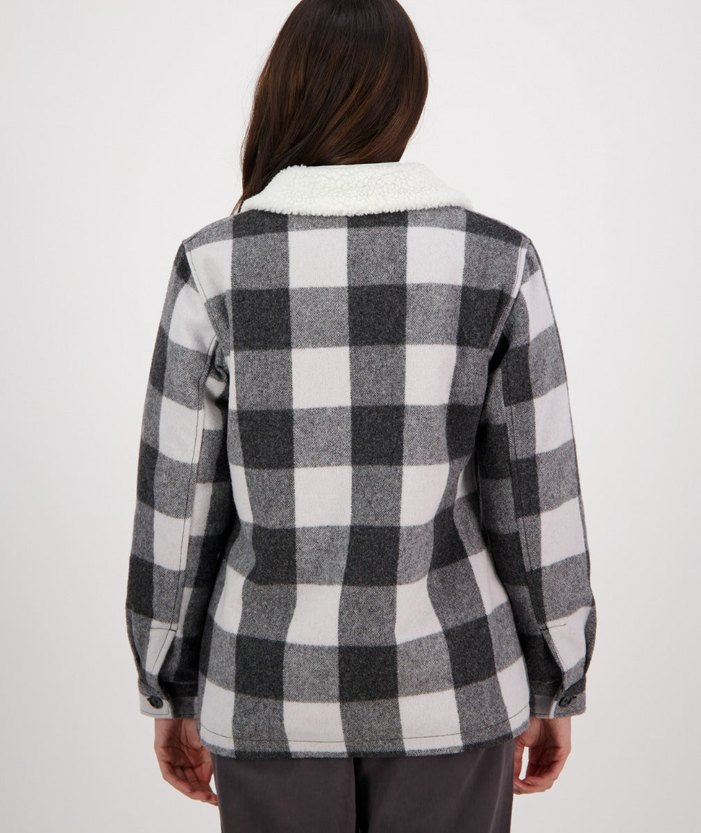 A person wearing a Swanndri Capitola Sherpa Jacket featuring a black and white checkered pattern and a white fleece collar is photographed from behind. The jacket, reminiscent of classic Wool Merino styles, has buttoned cuffs and is paired with dark pants. The background is plain white.