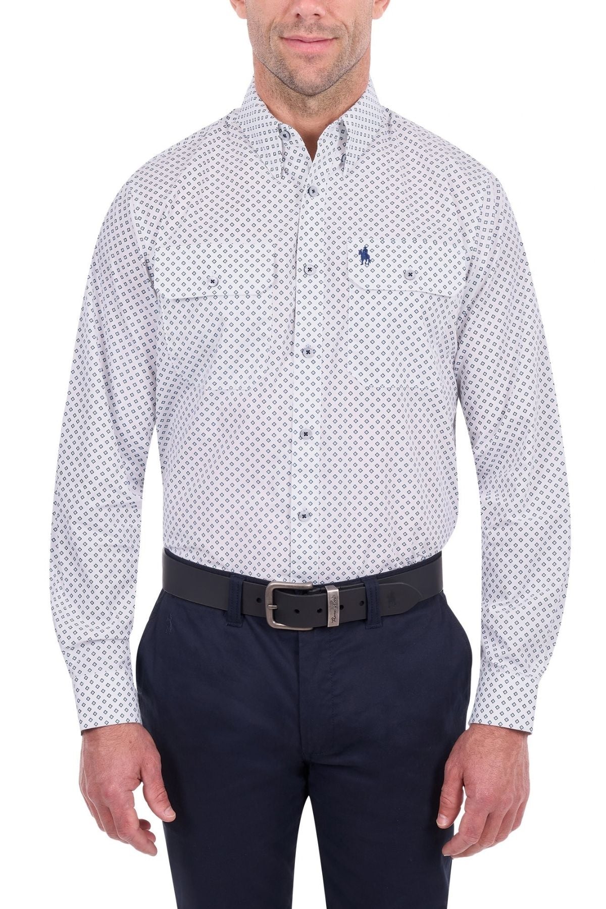 A man wearing the Thomas Cook Albie Shirt—a 100% cotton white button-up with a small blue pattern—paired with dark pants and a black belt, stands against a white background.