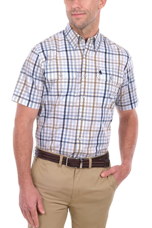 A man wearing the Thomas Cook Alfie Short Sleeve Shirt—a blue, brown, and white check, button-up cotton shirt—paired with tan pants and a brown belt. One hand is in his pocket while the other rests by his side.