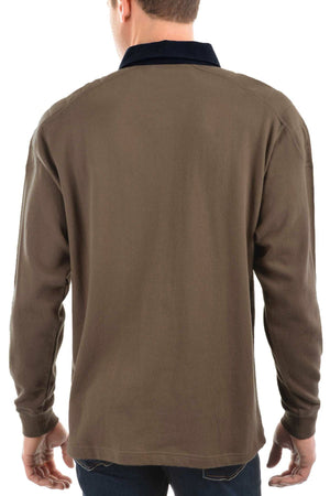A man is seen from behind wearing the Thomas Cook Bill Rugby, a brown cotton shirt with a dark collar, paired with blue jeans. His hands rest by his sides against a white background.