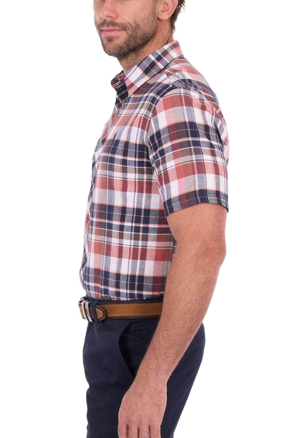 A man wearing the Thomas Cook Ethan Short Sleeve Shirt in a red, white, and blue plaid cotton-linen blend, paired with navy pants and a brown belt, stands sideways against a white background.