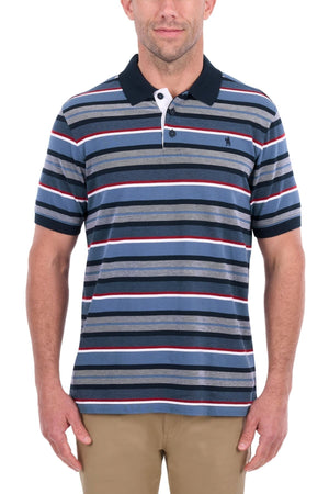 A man stands against a white background wearing the Thomas Cook Glenn Polo, a short-sleeve shirt with blue, gray, red, and white stripes and a dark collar, paired with beige pants.