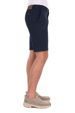 A person shown from the side against a white background wears navy blue Thomas Cook Harrison Shorts, beige slip-on shoes, and a white shirt. The Harrison Short is crafted with stretch fabric for added comfort and ease of movement.