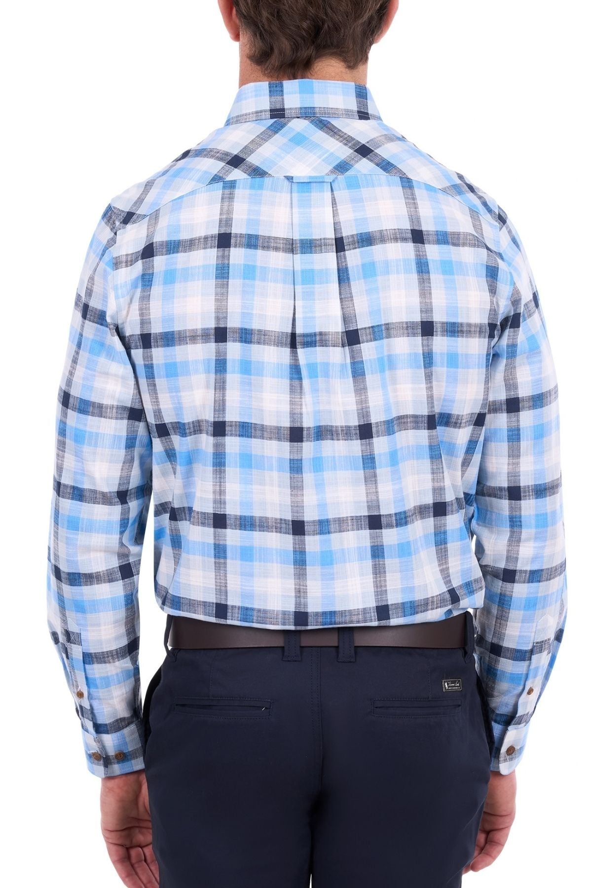 A man stands with his back to the camera, wearing a blue and white plaid long-sleeve Thomas Cook Jacob Shirt—an outback shirt crafted from 100% cotton—and dark navy pants.