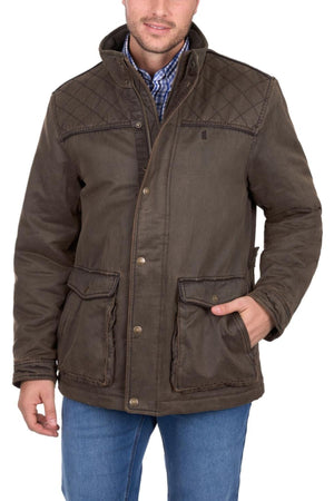 A man wears the Thomas Cook Marcus Jacket—a brown sherpa-lined faux oilskin coat with large front pockets—over a blue plaid shirt and blue jeans. Only his torso and lower face are visible, with one hand in his pocket.