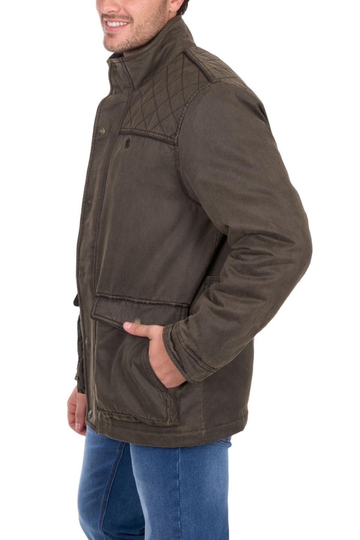 A man smiles against a plain white background, wearing the Thomas Cook Marcus Jacket in olive green with quilted shoulders and large front pockets, paired with blue jeans.