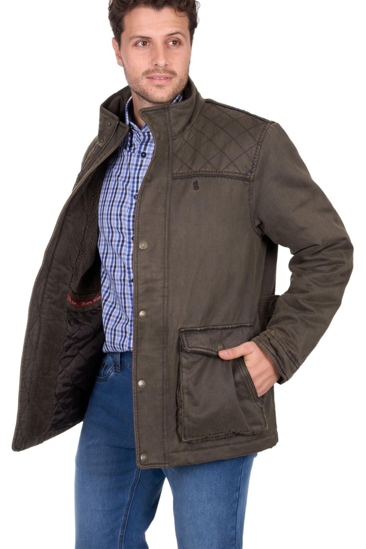 A man showcases the inner lining of a Thomas Cook Marcus Jacket, styled over a blue plaid shirt and blue jeans, with one hand in his pocket.