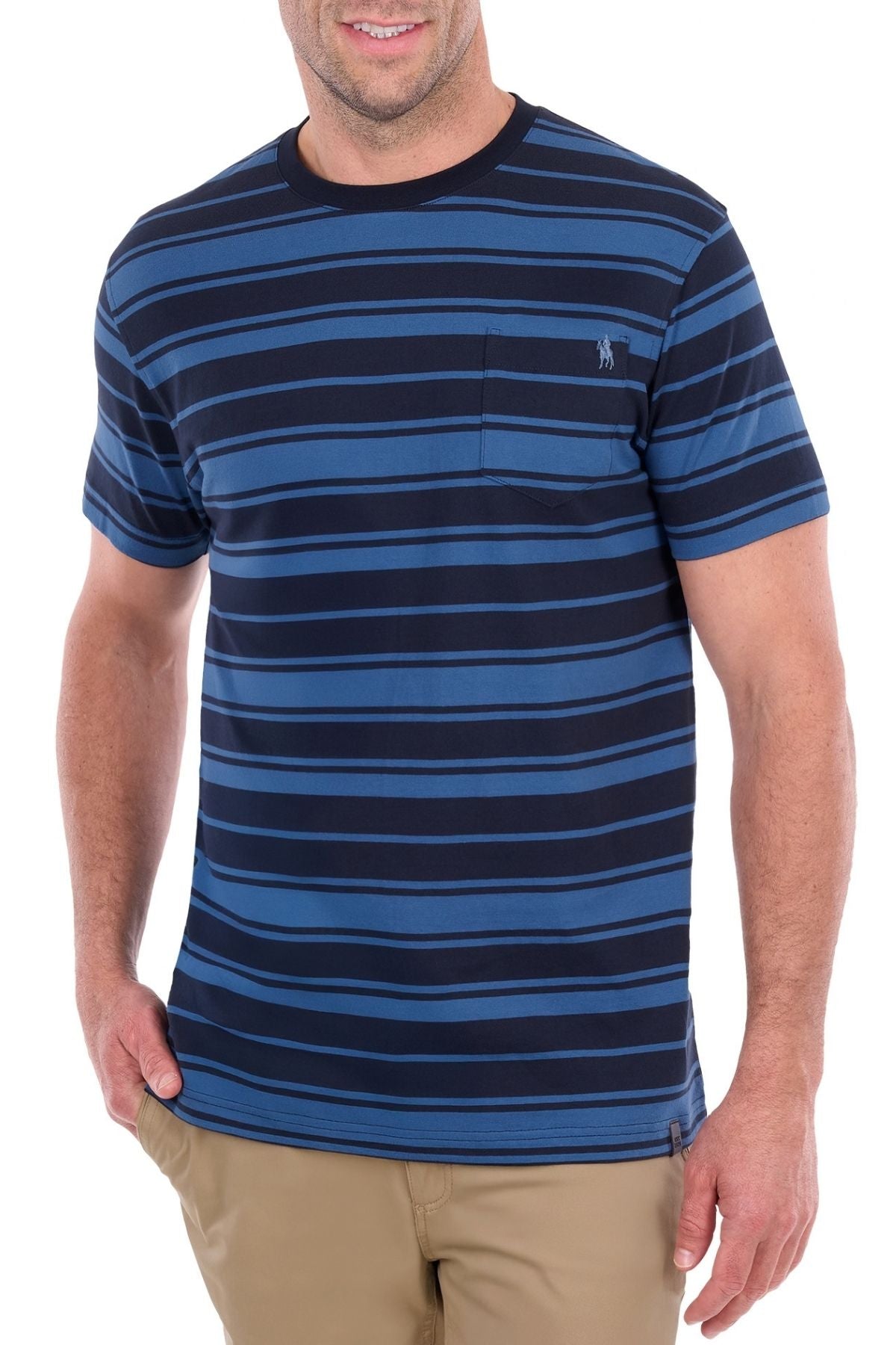 A man wearing the Thomas Cook Pete Tee—a short-sleeve blue and navy striped shirt crafted from soft cotton jersey with a chest pocket—paired with tan pants, stands with one hand in his pocket and smiles.