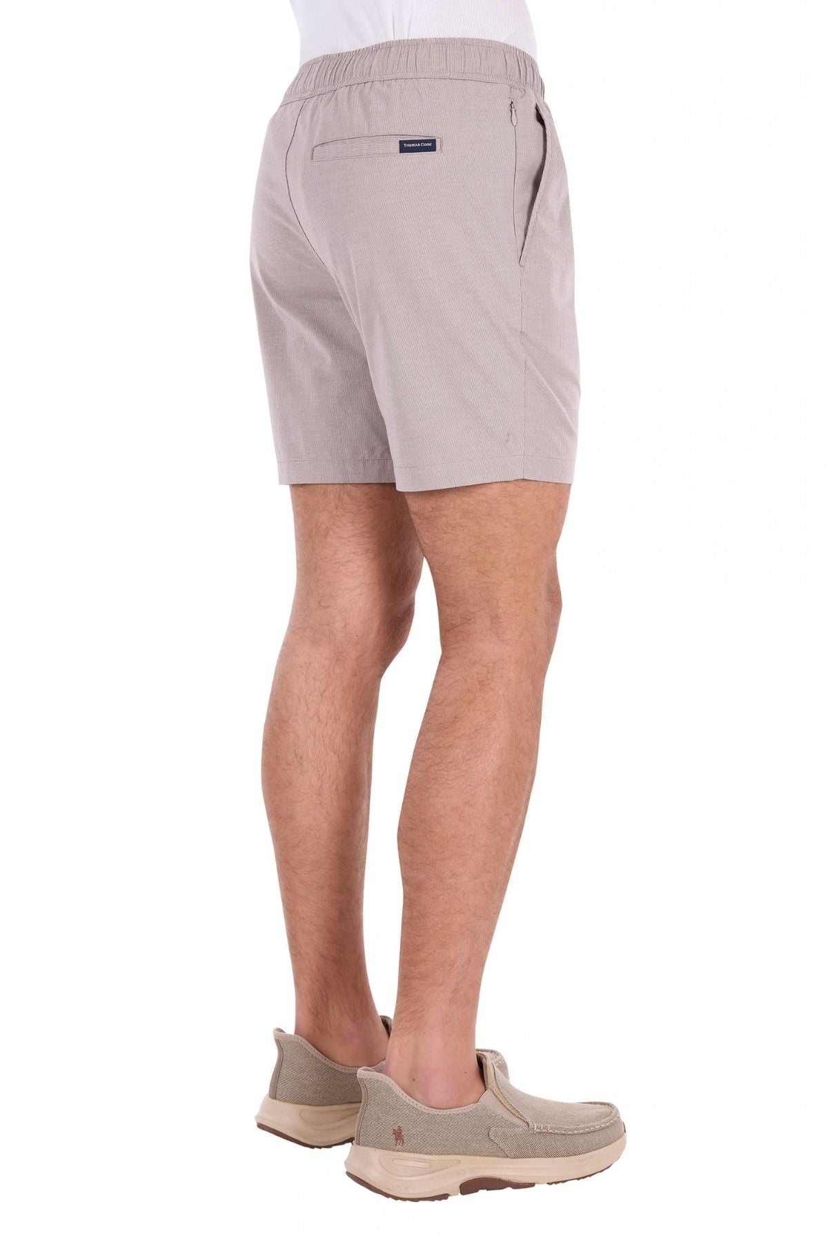 A person wearing the Thomas Cook Rowan Short in light beige, crafted from premium textured fabric with stretch technology, stands facing away, displaying the back and side view of the shorts against a white background.