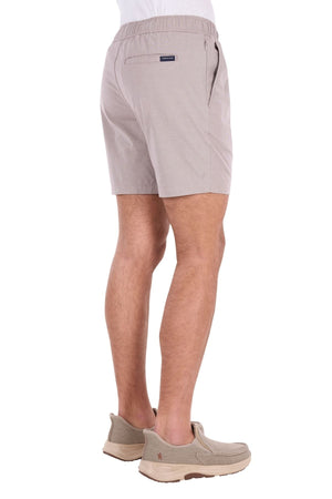 A person wearing the Thomas Cook Rowan Short in light beige, crafted from premium textured fabric with stretch technology, stands facing away, displaying the back and side view of the shorts against a white background.