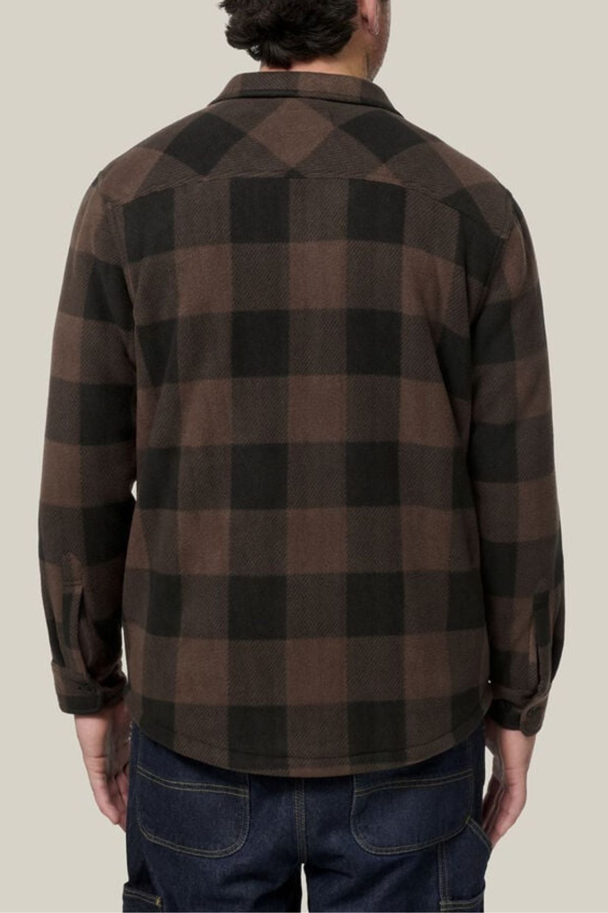 A person stands with their back to the camera, wearing the Hard Yakka Legends Sherpa with FREE Beanie—featuring a brown and black plaid flannel design, fleece body lining, and dark jeans against a plain light background.