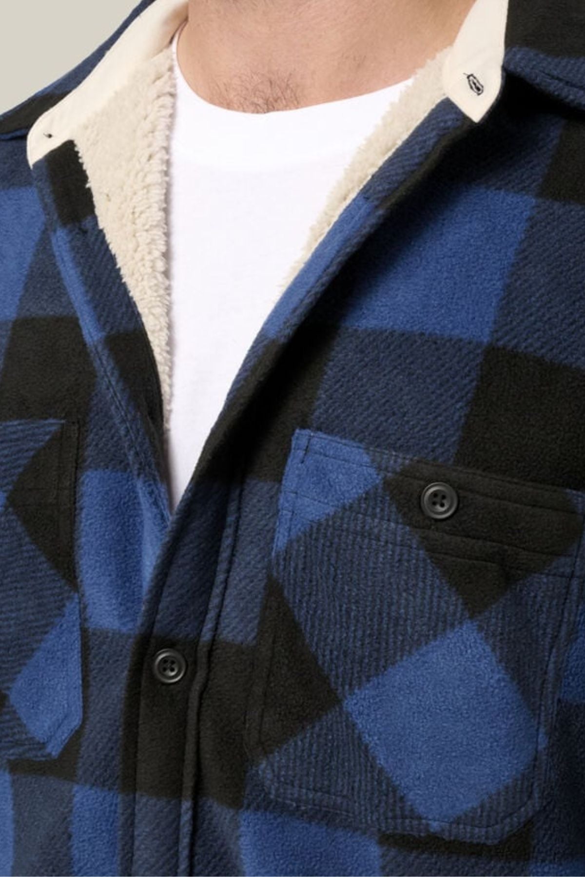A close-up of a person wearing the Hard Yakka Legends Sherpa with FREE Beanie—blue and black plaid shirt with black buttons, cream fleece lining for thermal insulation, and layered over a white T-shirt with visible collar lining.