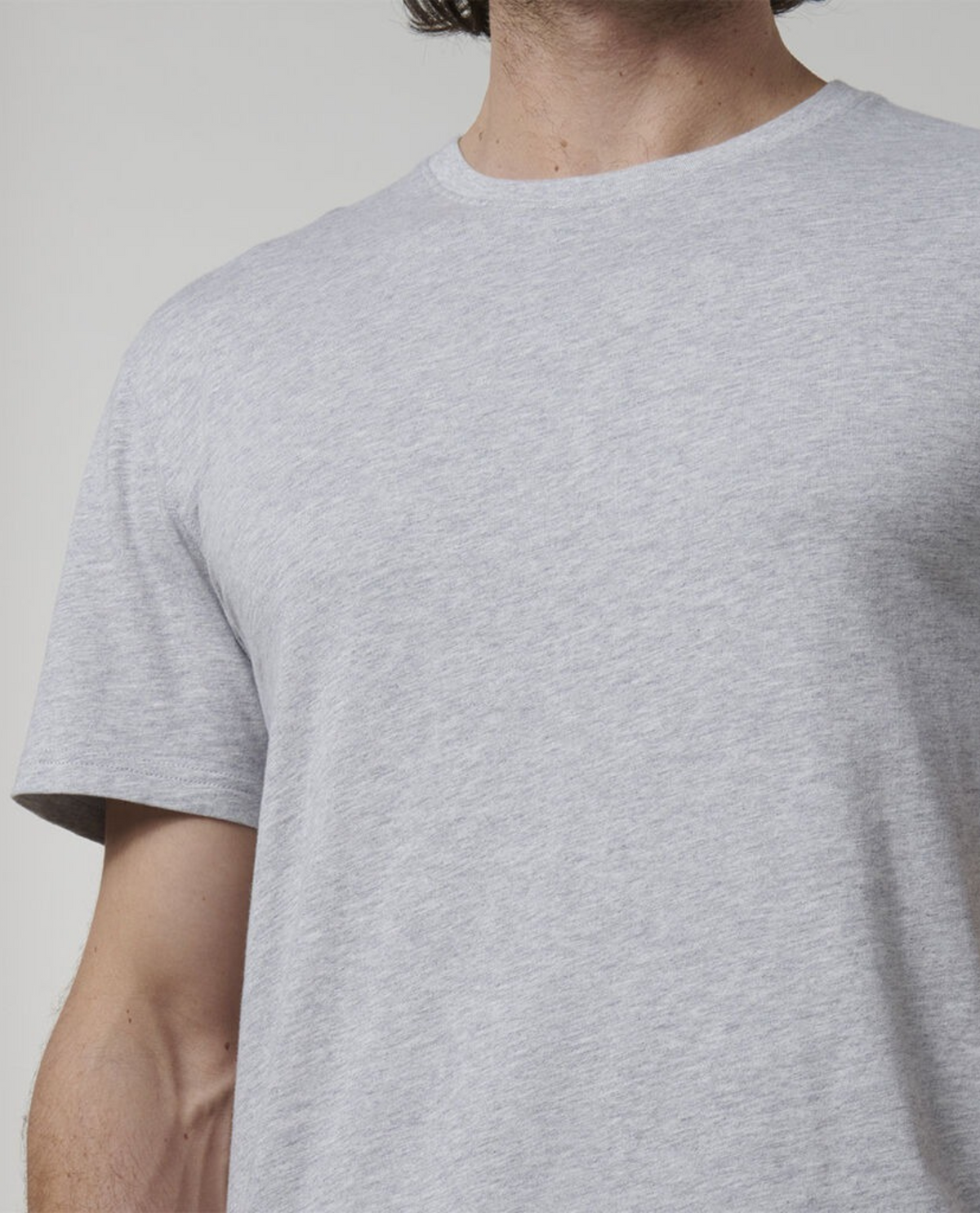 A close-up shot captures a person donning the light grey Hard Yakka Core Tee, fabricated from 100% Cotton. The focus is on the upper torso, part of the right arm, and a section of the neck, likely featuring fabric sourced from Australian Cotton farms. The backdrop is plain and neutral.