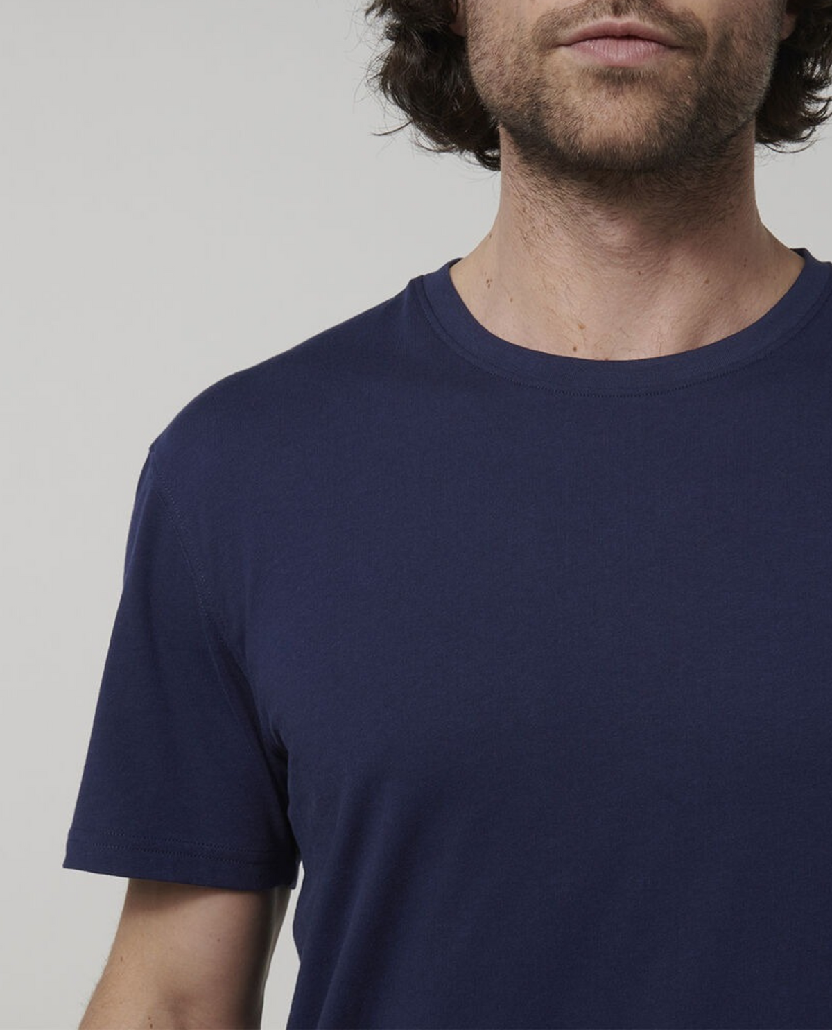 A man wearing a Hard Yakka Core Tee in plain navy blue, made from 100% Australian cotton, is shown from the shoulders up against a neutral background. The image captures part of his face but emphasizes the t-shirt's premium quality which originates from Australian cotton farms.