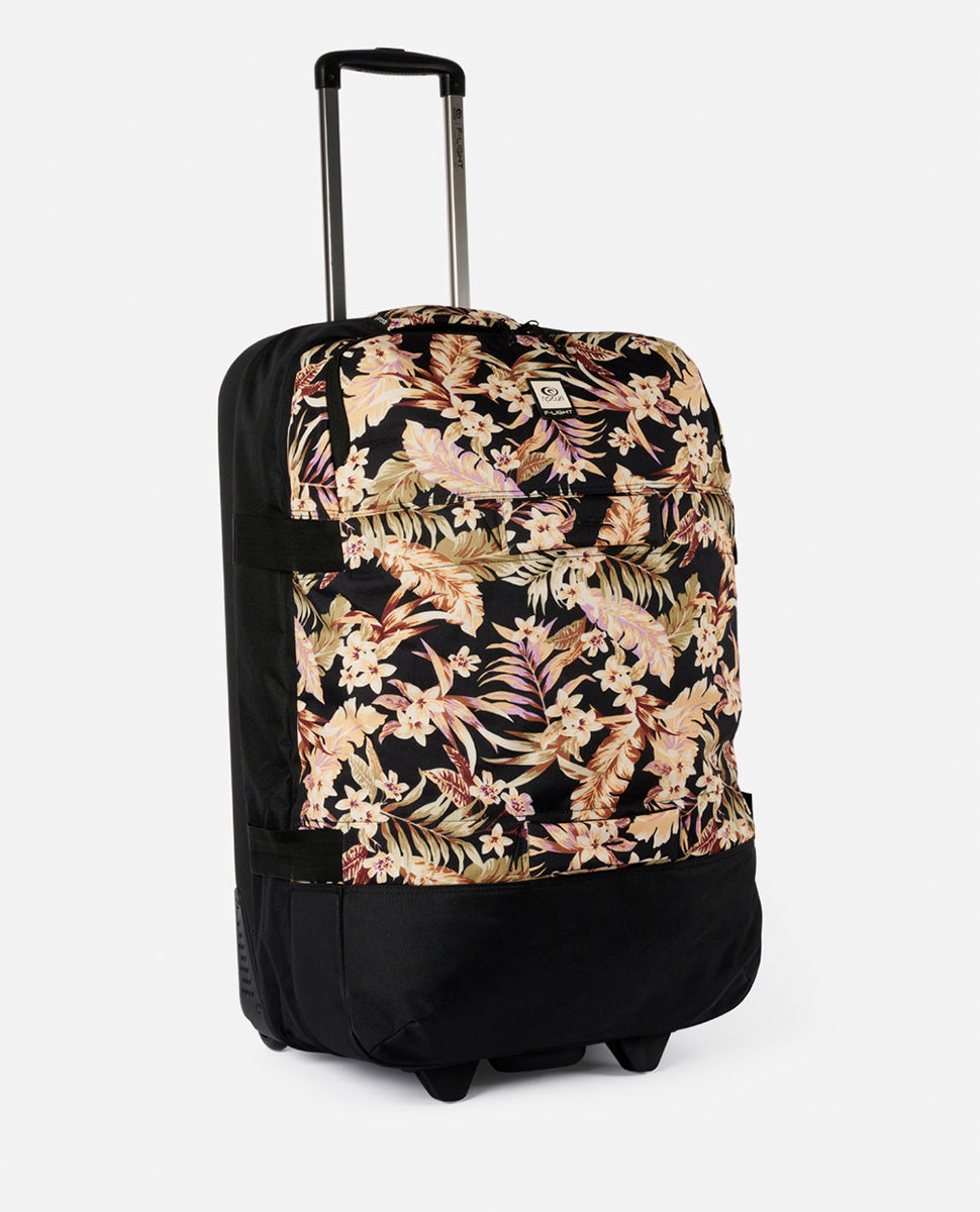 The Rip Curl F-Light Global 110L Sunday Travel Bag is a wheeled travel bag featuring a black base with a floral pattern of beige and pink flowers on an external pocket. It includes lockable zips, an extended telescopic handle, and two wheels for easy transport.