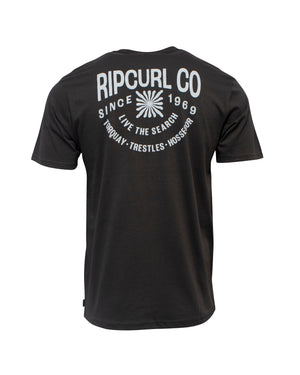 The Rip Curl Cosmic Burst Tee is a black 100% cotton T-shirt featuring "RIP CURL CO SINCE 1969 LIVE THE SEARCH TORQUAY • TRESTLES • HOSSEGOR" and a circular white back print—ideal for casual style.