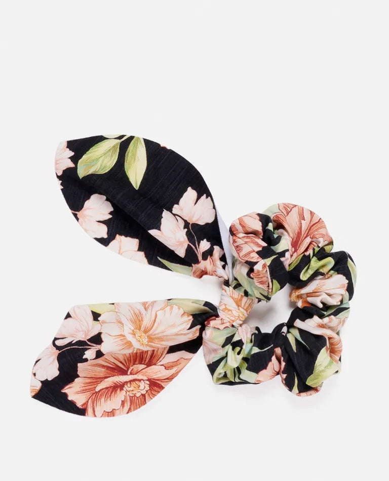 The Rip Curl Sol Seeker Bow Scrunchie showcases a chic floral design with pink and peach flowers on a black background. This ruffled, elastic scrunchie is crafted to stylishly secure your hair, featuring an attached bow for extra flair.