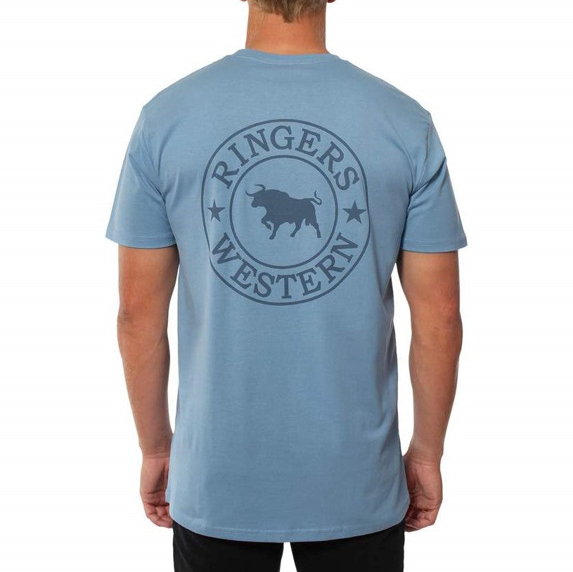 A person wearing a light blue Ringers Western Signature Bull Original Fit T-Shirt with a circular design featuring a bull on the back. The individual, dressed in black pants and facing away from the camera, showcases this comfortable 100% cotton tee.