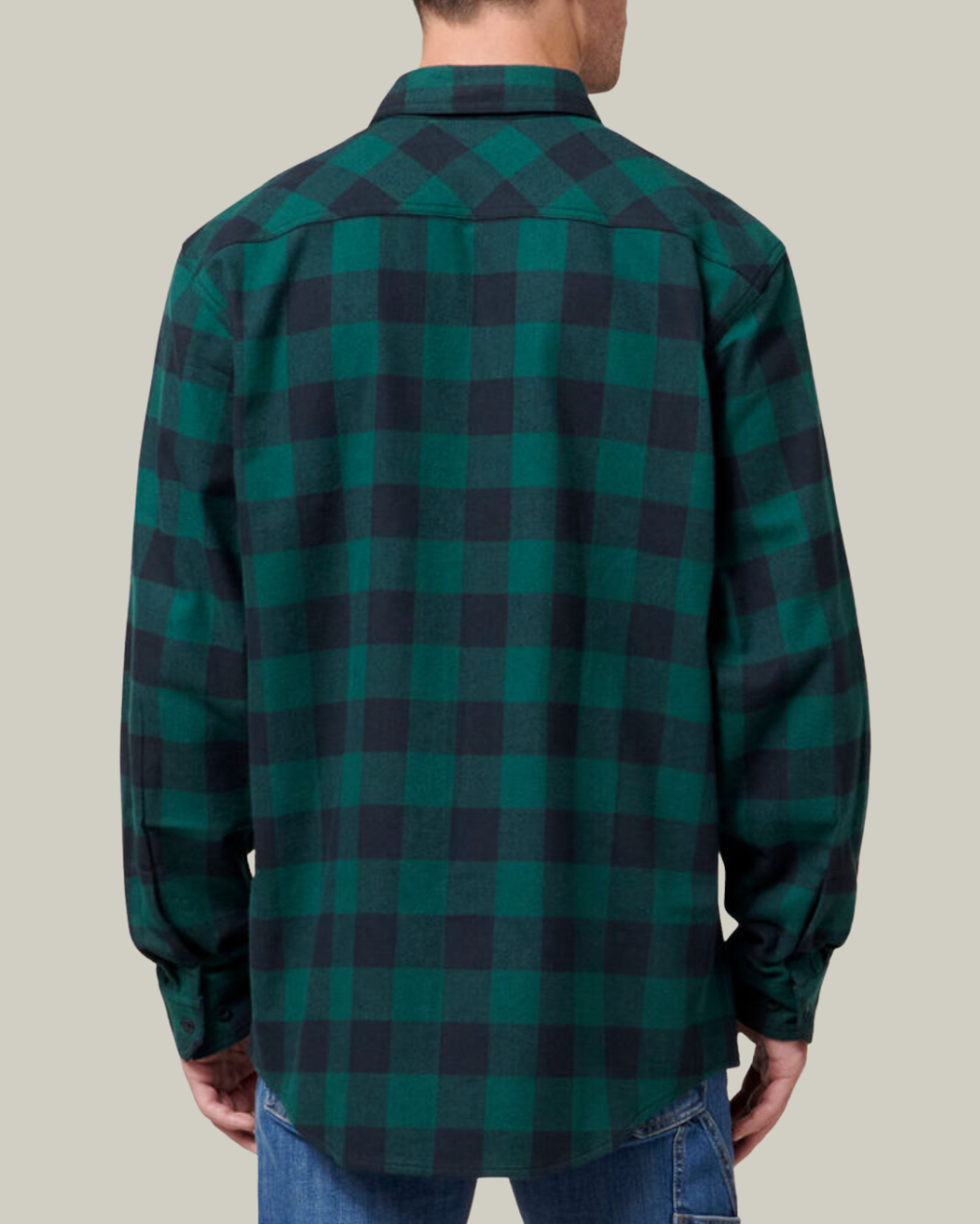 A person is seen from the back wearing a Hard Yakka Check Flannelette Shirt in green and black plaid cotton twill with long sleeves, paired with blue jeans, against a plain beige background.