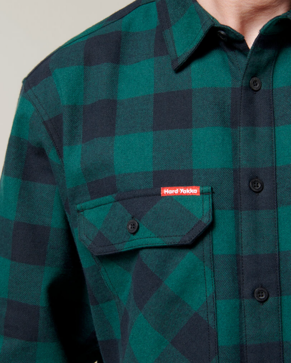Close-up of a person wearing the Hard Yakka Check Flannelette Shirt, made from durable cotton twill in green and black checks, featuring black buttons and a front pocket with a small red "Hard Yakka" label.
