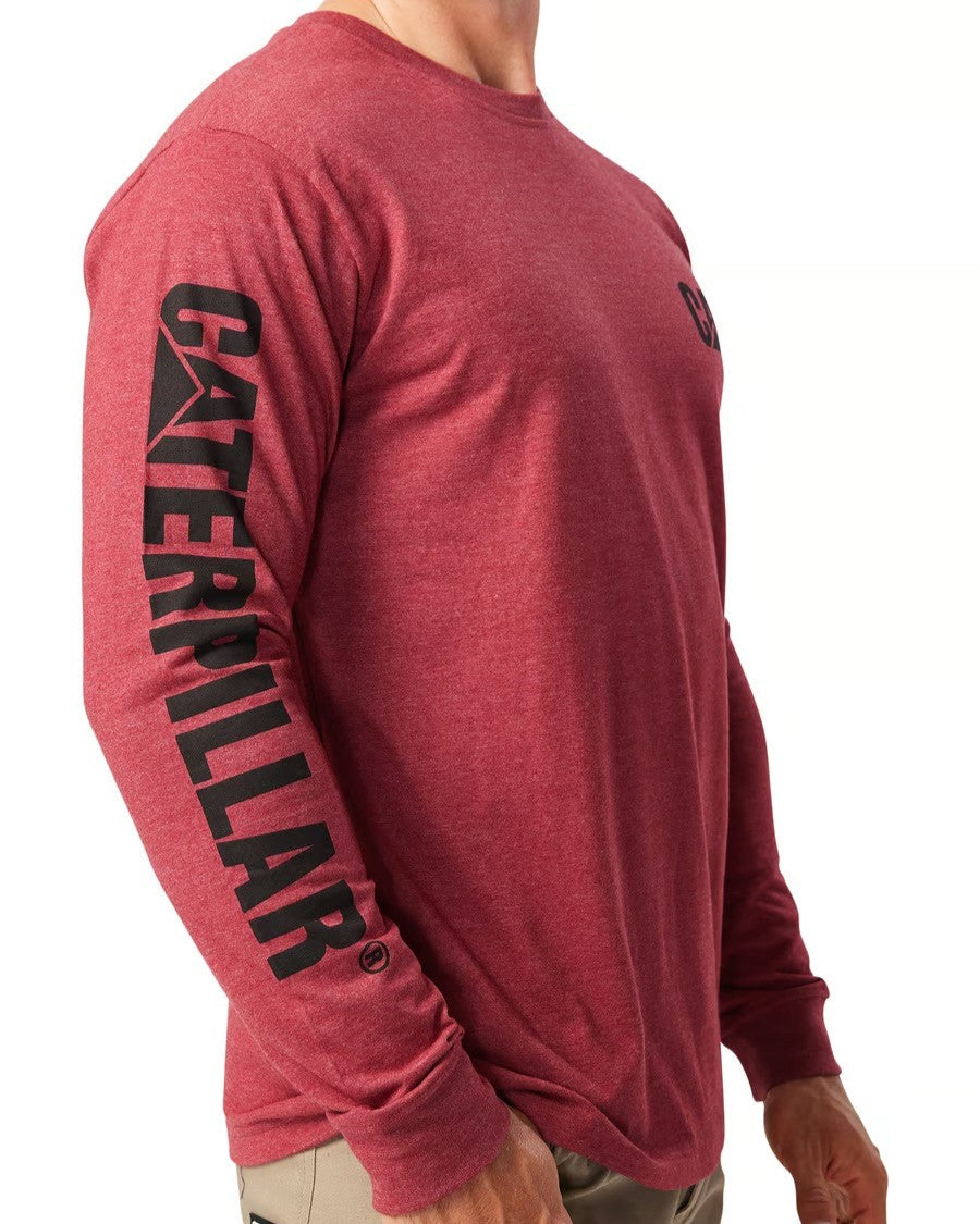 The individual is wearing a relaxed-fit CAT Trademark Banner Long Sleeve Tee in red, featuring "Caterpillar" printed vertically in black on the sleeve, with their arms casually resting by their sides.