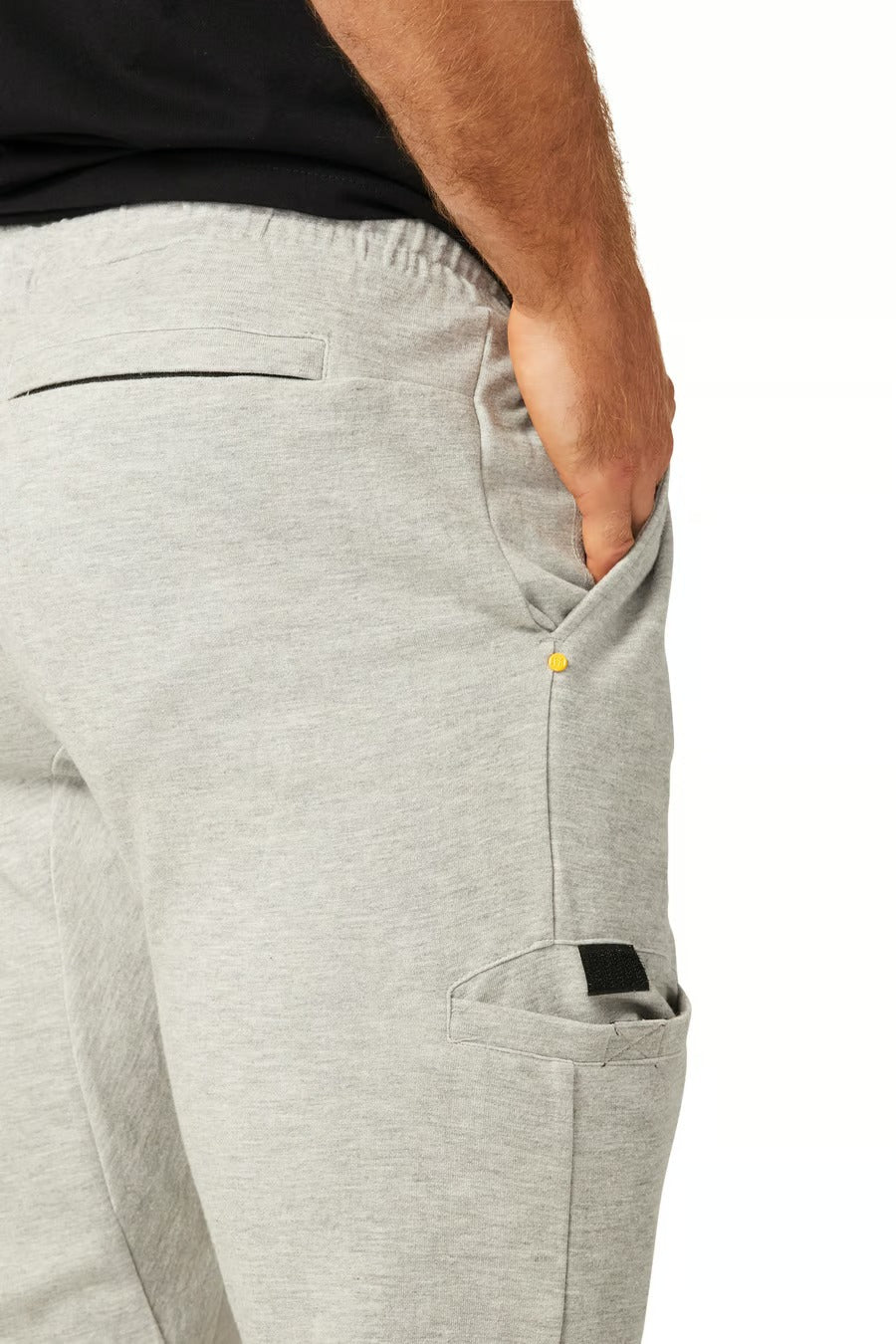 Sporting CAT Track Pants in light grey, one hand rests in the right pocket. The pants have a small black and yellow accent and a sturdy cargo side pocket against a plain white background.