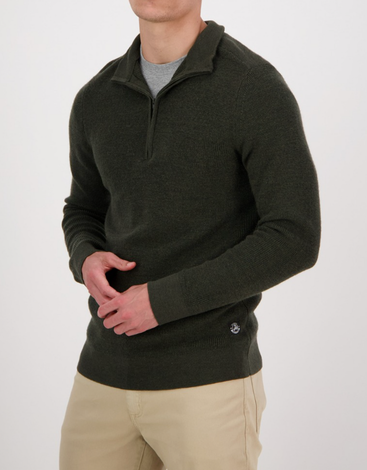 Wearing a Swanndri Magnet Bay v2 dark green Merino jumper with a half-zip collar over a gray shirt and beige pants, the person stands against a plain white background, with their face not visible.