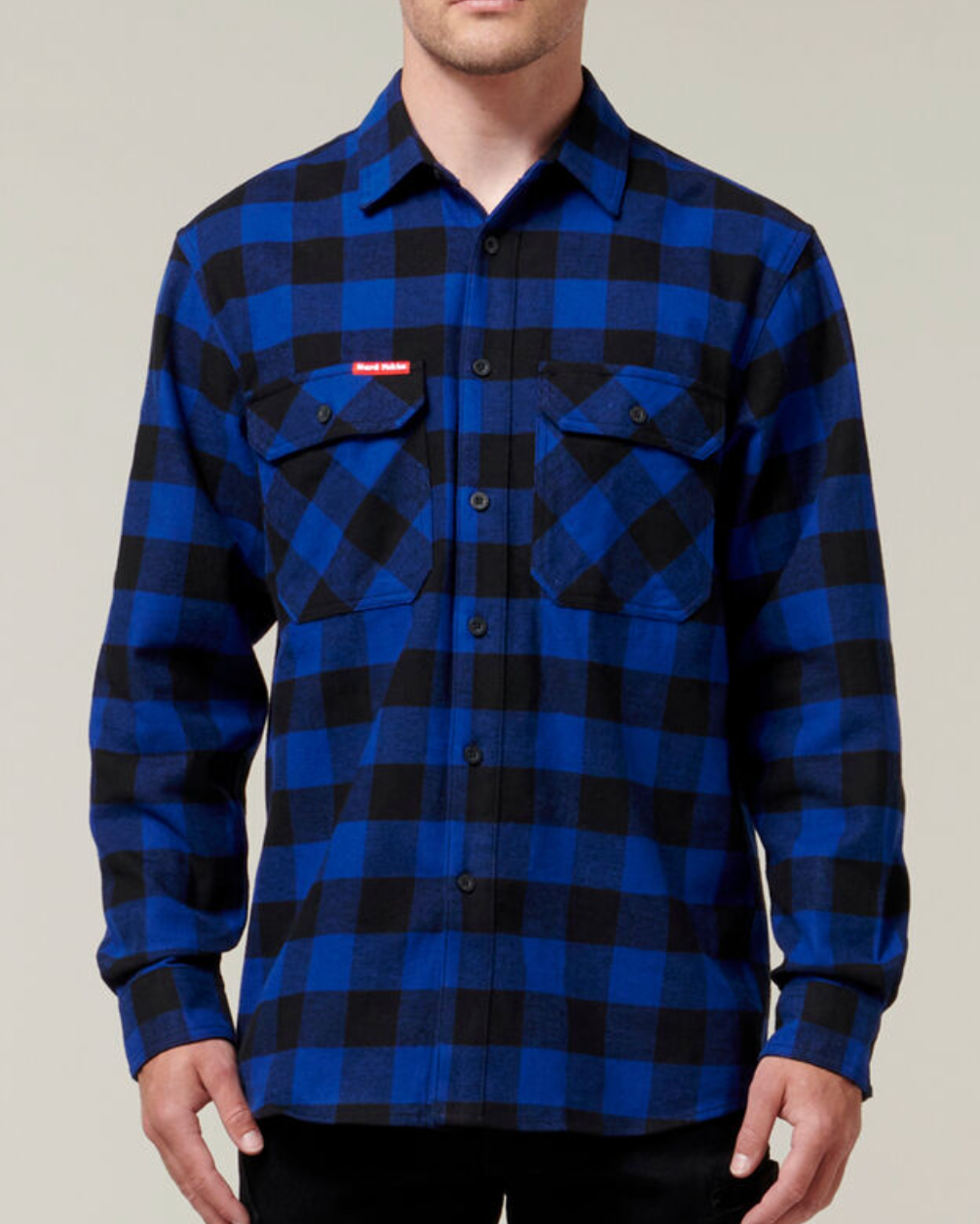 A person is wearing a Hard Yakka Check Flannelette Shirt in blue and black with buttoned chest pockets and a small red patch on the left chest. This durable shirt, crafted from Cotton Twill, is buttoned up and provides UPF 50+ sun protection. The person is shown from the shoulders to the waist against a neutral background.