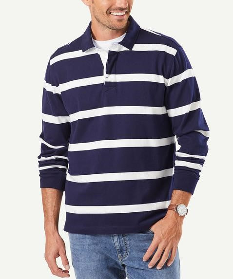 A person wearing a stylish Gazman Classic Stripe Rugby in navy blue and white horizontal stripes is smiling. They are also wearing light blue jeans and a watch on their left wrist, exuding comfort against the plain white background.