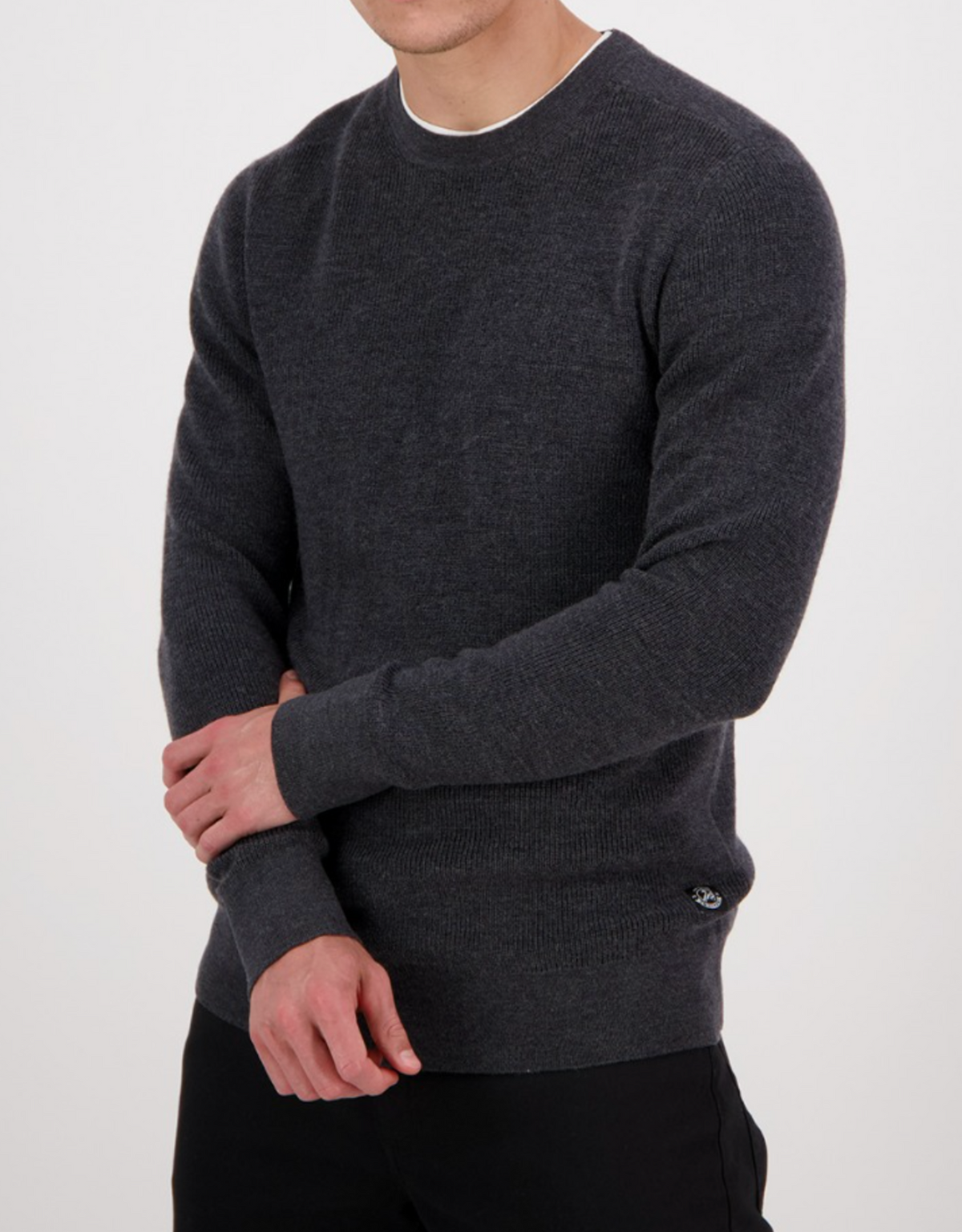 A person stands facing forward in the Swanndri Otahu River Crew Neck Merino Knit, dark gray with long sleeves, paired with black pants. Arms are slightly crossed; head is partly out of frame. Plain white background provides a clear size reference.